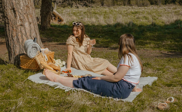 a girl sits under trees enjoying a British summer picnic