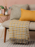 A gold spotted milan merino lambswool blanket is thrown on a beige sofa in a living room scene