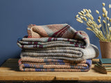 a stack of rustic cosy recycled blankets sit on a wooden bench