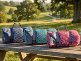 Four woven british picnic blankets on a wooden table with a scenic background
